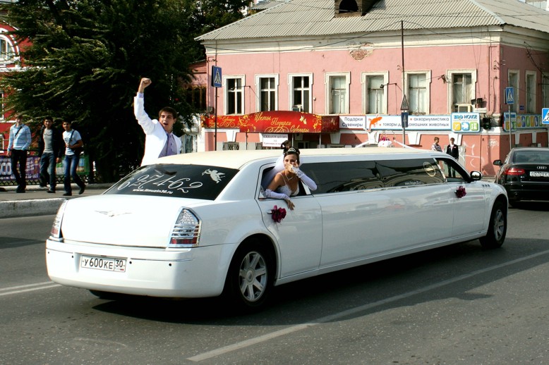 Newly married couple waving to passers-by from a wedding limousine Newly married couple waving to passers-by from a wedding limousine